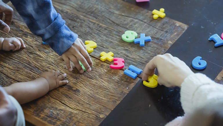 Kids engaging with colorful plastic numbers on a wooden table, fostering early math skills.